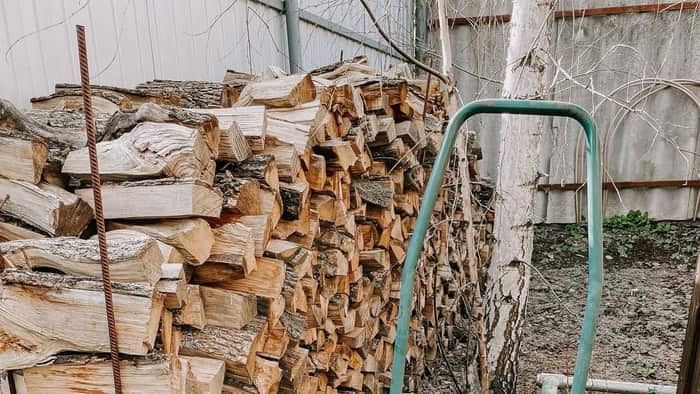 Neatly stacked firewood beside a wheelbarrow in a backyard, ready for a delivery receipt to be checked